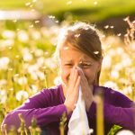 Young girl blowing nose into tissue, standing in a field.