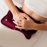 Woman sitting down, holding heating pad over belly.