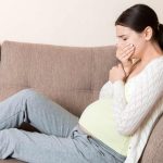 Pregnant woman on couch holding mouth, trying not to vomit.